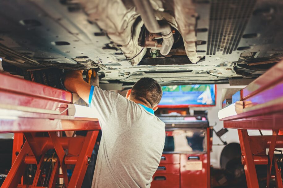 A mechanic working on a car engine in a well-lit auto repair shop.